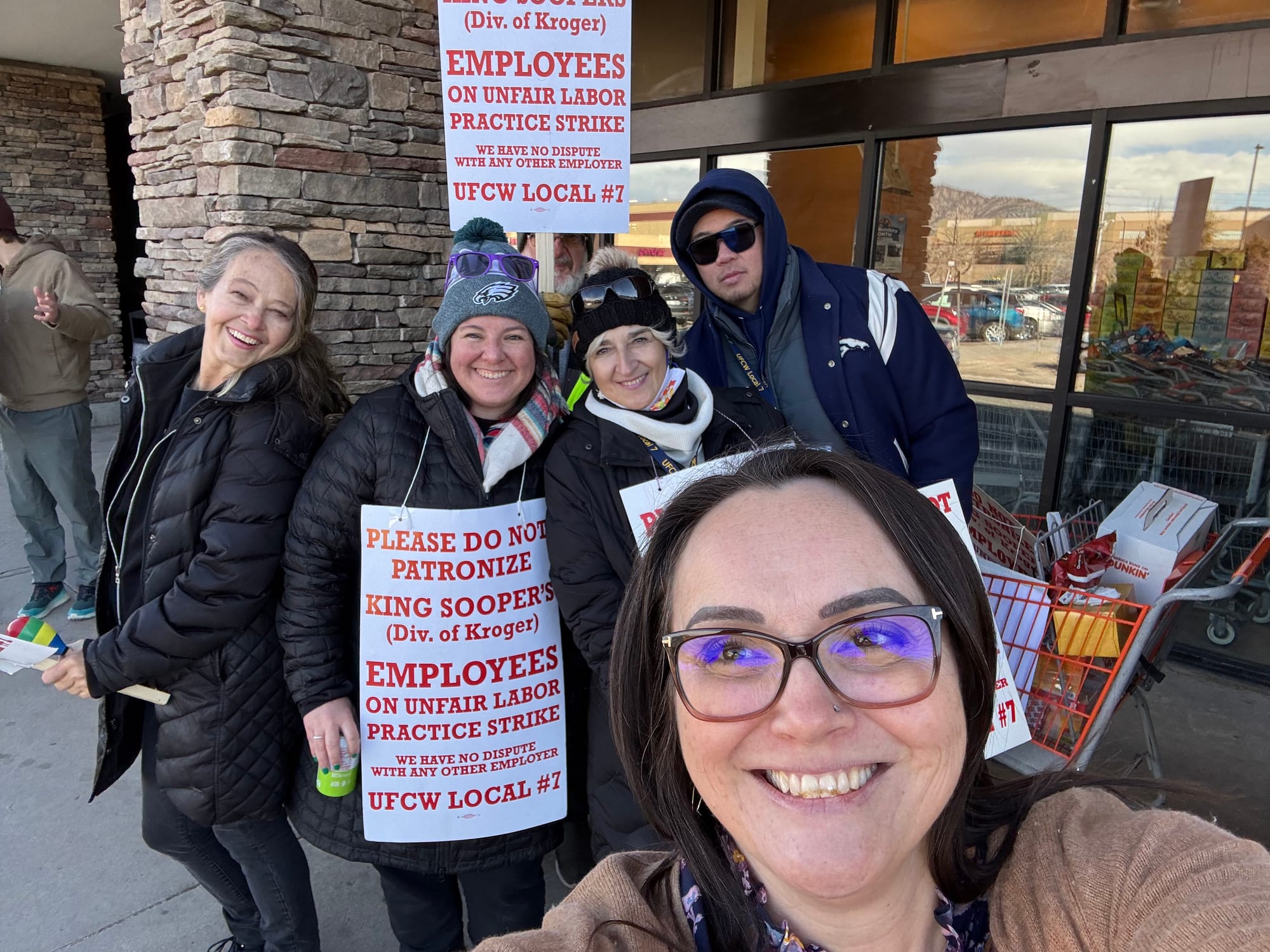 Four workers and Nicole smile at the camera while standing outside of a King Soopers store.