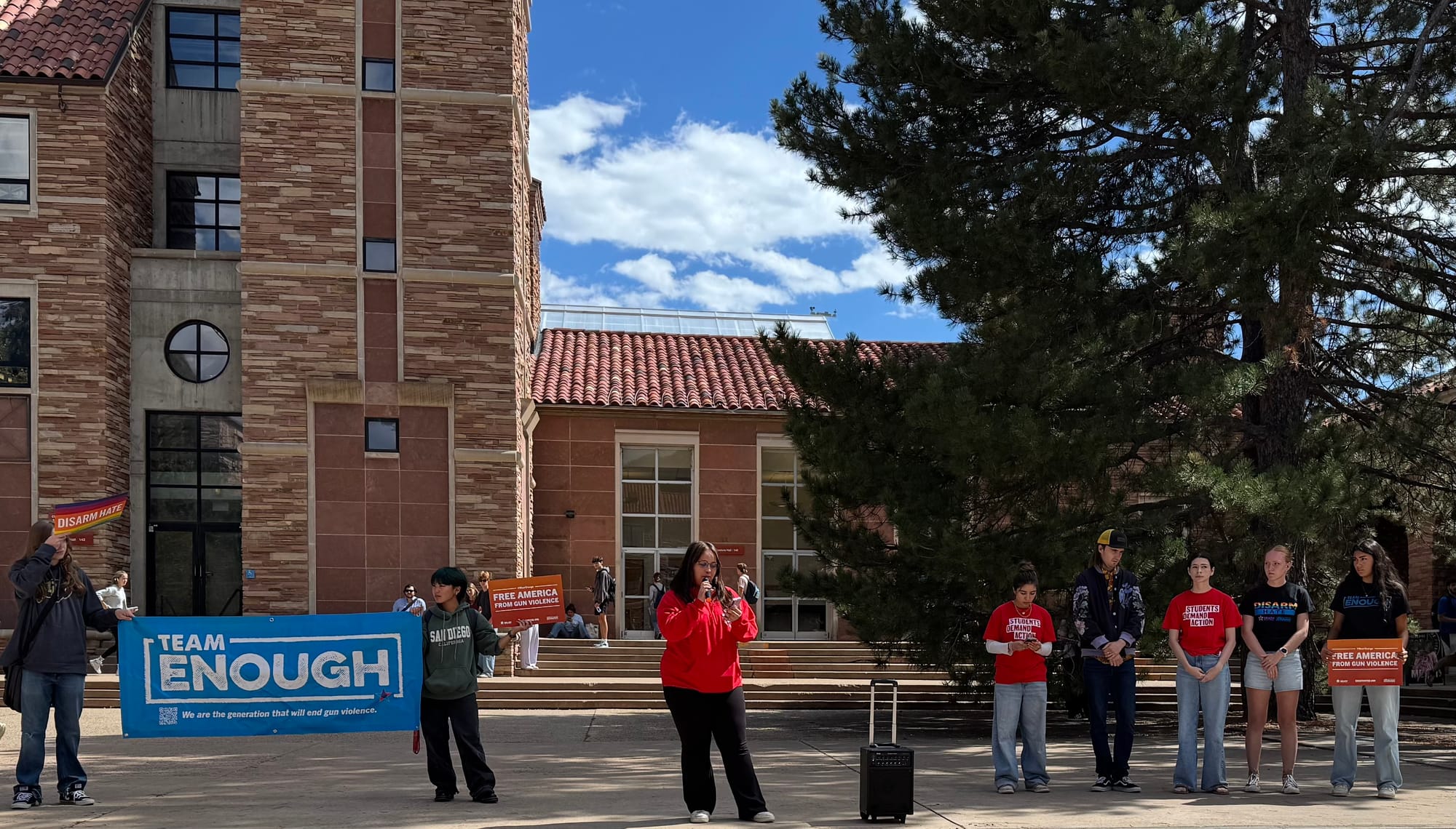 A student speaks into a microphone next to a blue banner that reads "TEAM ENOUGH."