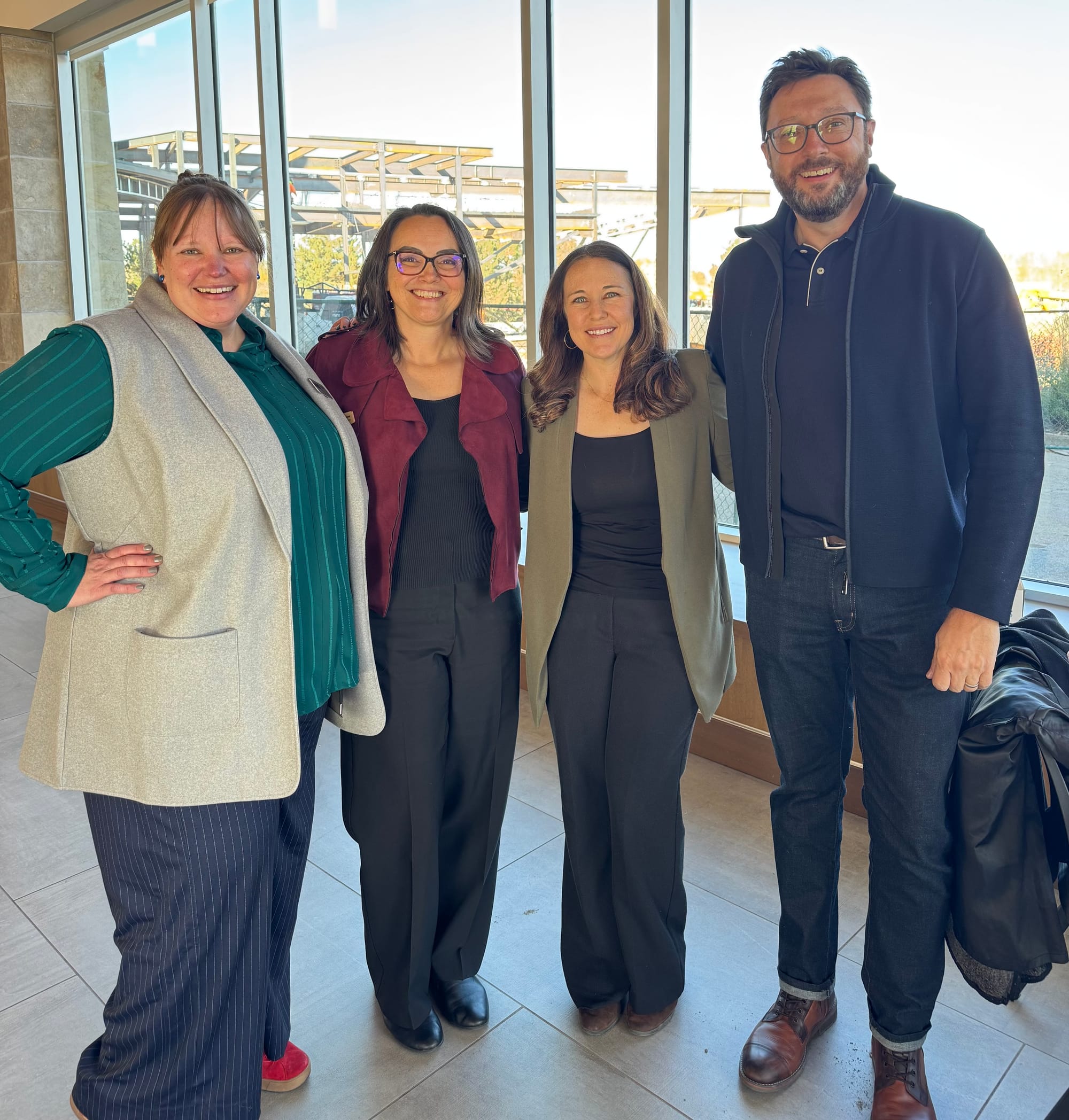 Four adults stand smiling in front of large windows at a professional gathering.