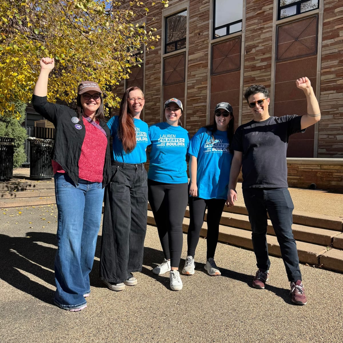 Five people smile and stand with raised fists in front of a stone building.