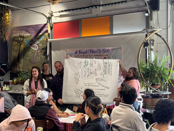 A small group of people speak to a larger group while holding a large drawing of their ideas.