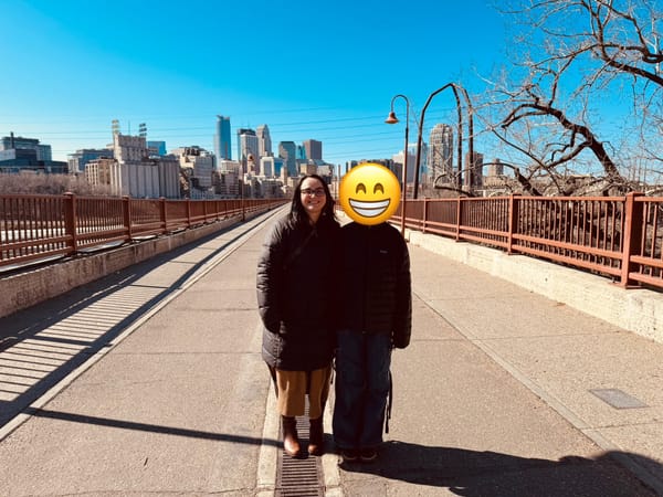 Nicole and her oldest child stand on the Stone Arch Bridge on a sunny day with downtown Minneapolis in the background.