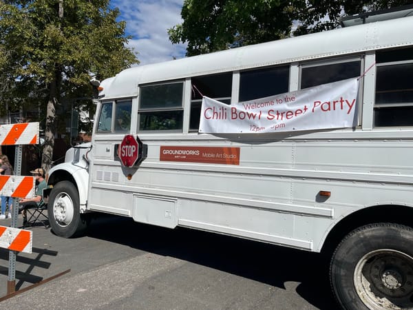A white bus blocks a street. An orange sign on the bus reads "Groundworks Art Lab Mobile Art Studio."