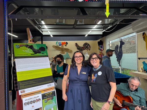 Two people in front of the entrance to an art studio where colorful art projects line the walls.