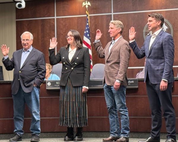Four people raise their right hands during a swearing-in ceremony at Boulder City Council chambers.
